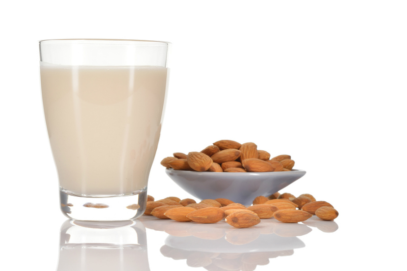 glass of almond milk with some almonds on a table
